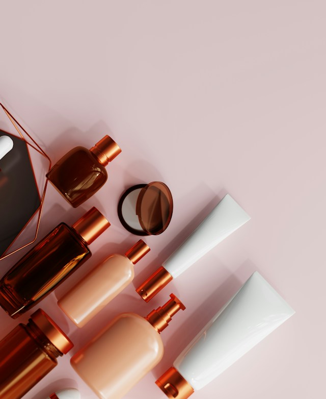 Amber glass bottles, copper-capped pumps and white tubes laid out on a soft pink surface