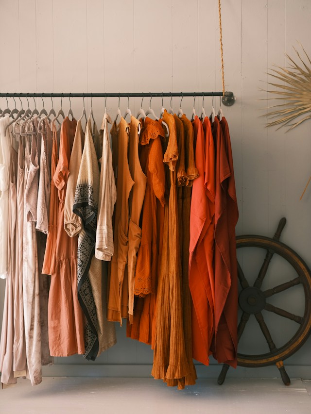 A rail of dresses and blouses in rust and cream tones against a pale wall