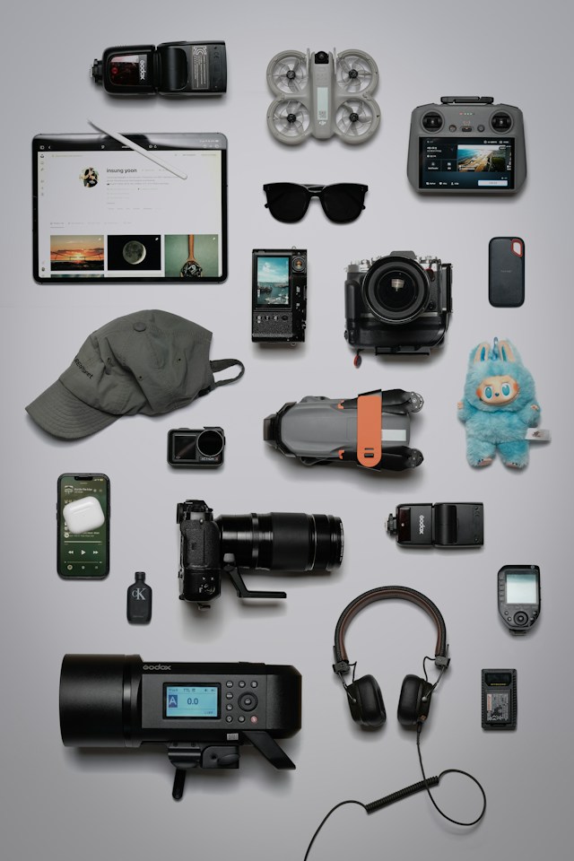 A flat lay of cameras, lenses, headphones, a tablet and other gear on a grey surface
