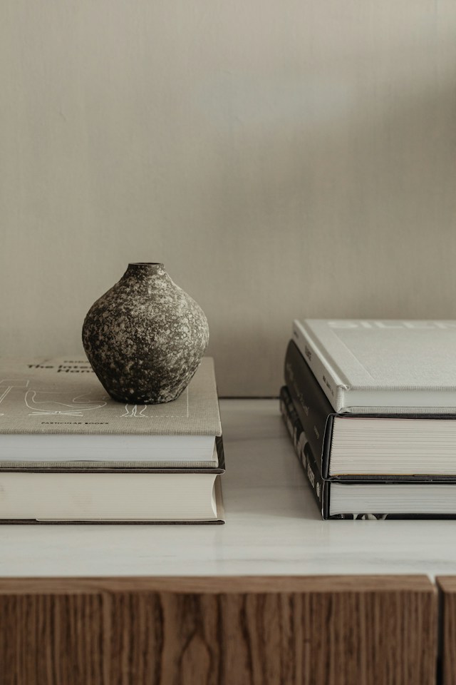Two stacks of hardback books on a marble top, with a speckled ceramic vase resting on one